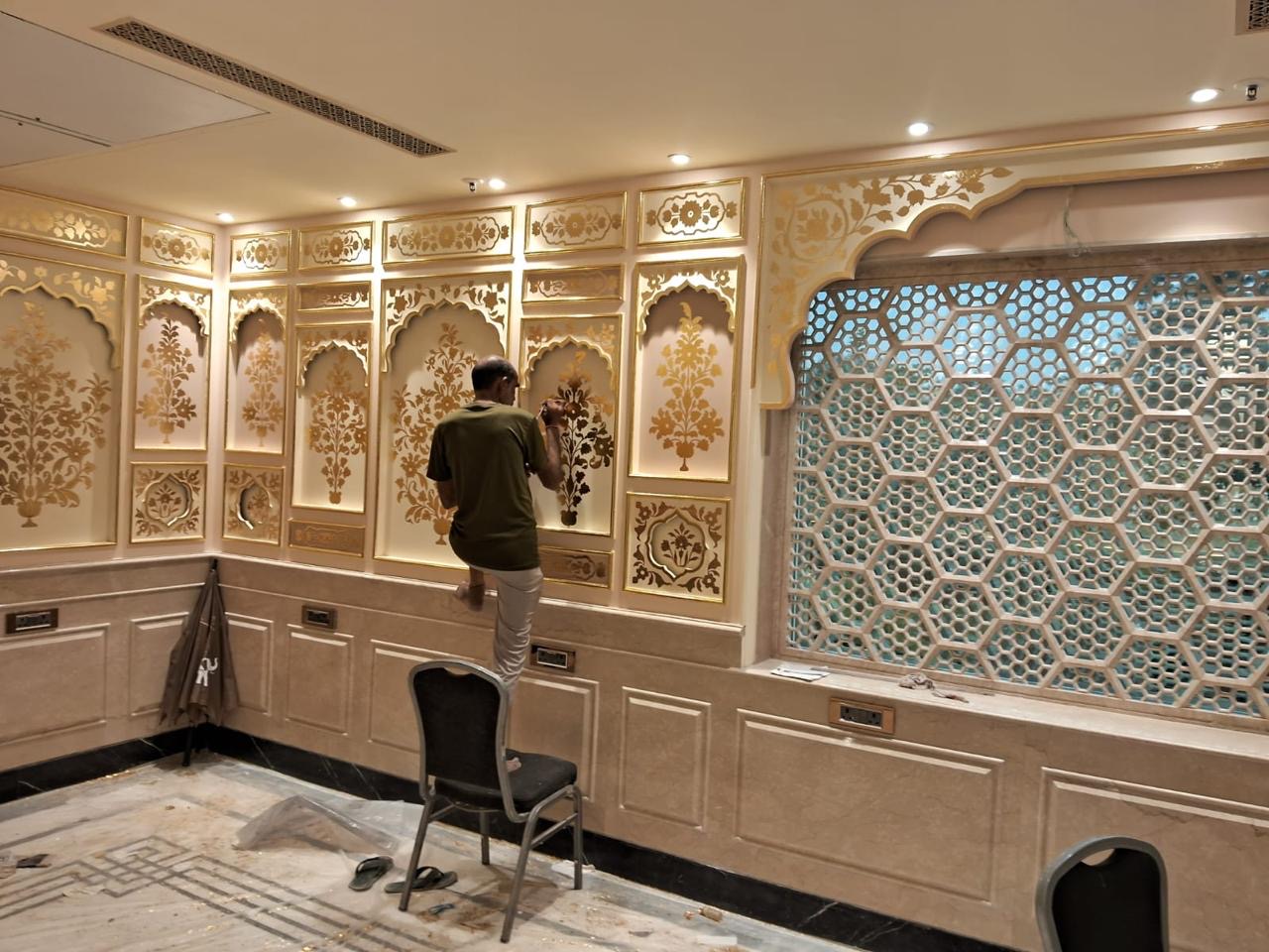 A StudioDarts artisan laying gold leaf by hand on carved floral wall panels